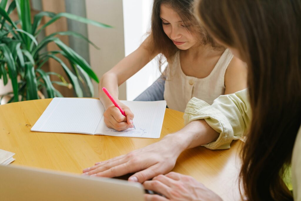 gas-pipeline A woman helping a young girl with a writing task at a wooden table, enhancing their learning experience.